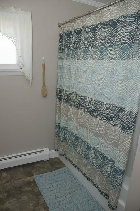 Multicoloured shower curtain hung on railing nearby blue bath mat